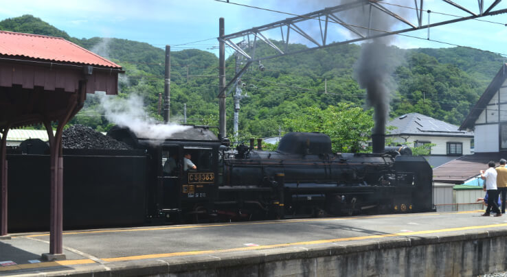 The steam locomotive departs while whistling loudly and puffing black smoke